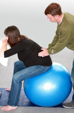 lady sat on a gymball, her lower back is being massaged