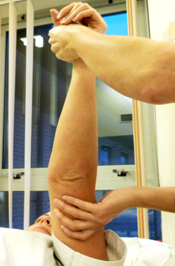Laying down, the hand is being held and supported under the upper arm, the arm is pointing straight up