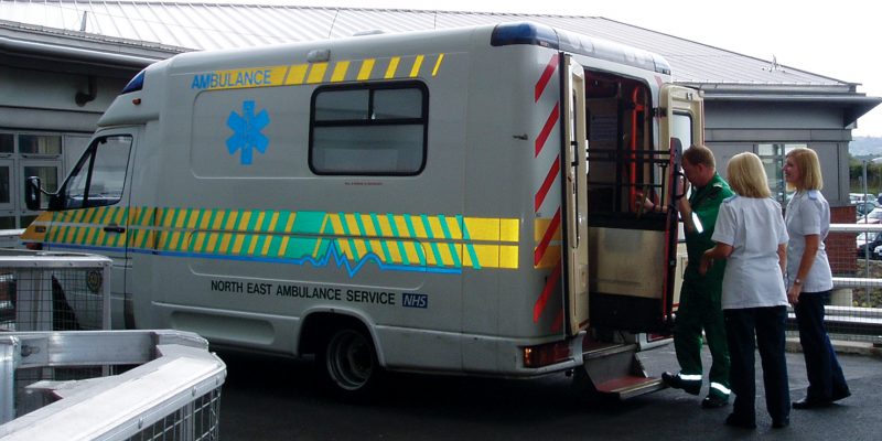 Photograph of an ambulance with a paramedic with the ambulance doors open and and nursing staff waiting to greet the patient.