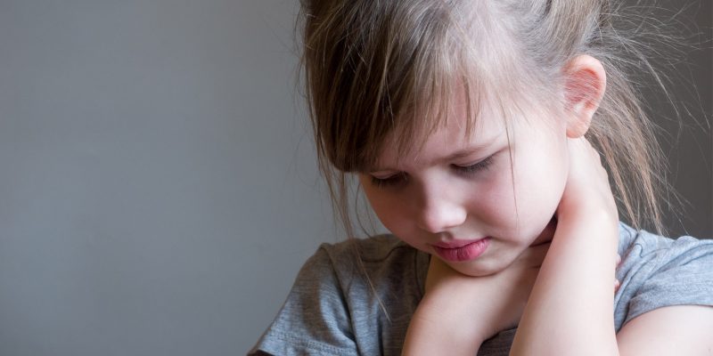 A young girl looking down holding her neck and collarbone in pain