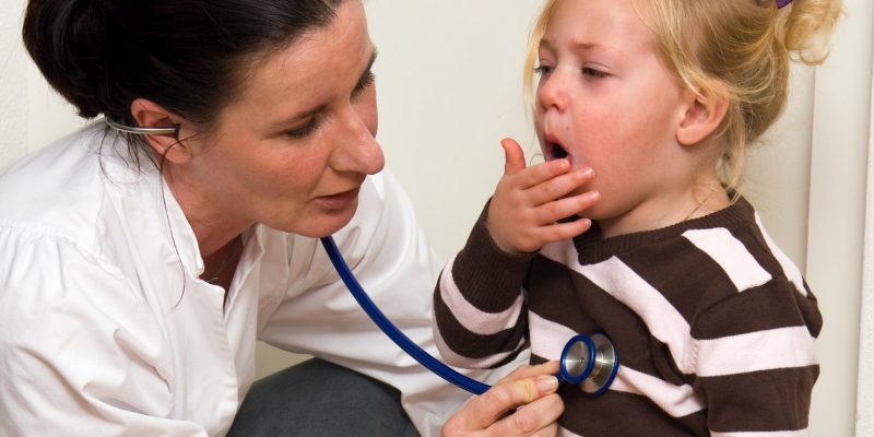 A health professional listening to a young childs' chest through their stethoscope. The child is coughing.