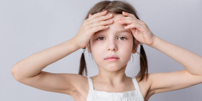 Photograph of a child with their hands on their forehead looking like they are in some kind of discomfort after suffering a head injury.