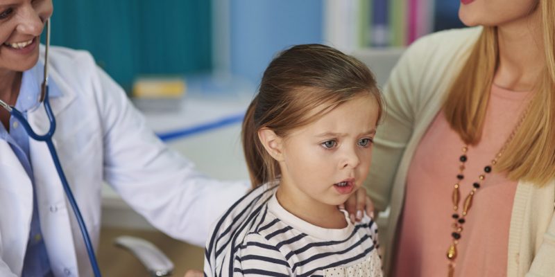 A doctor is listening to a young girls breathing through a stethoscope