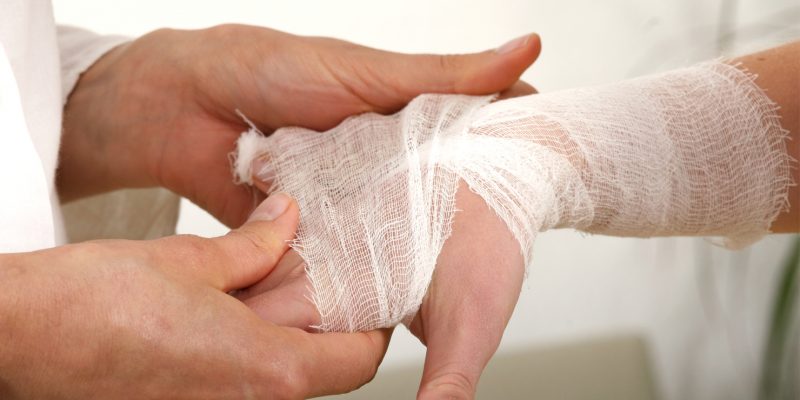 Image showing a health professional examining a patients hand, the hand has a dressing applied.