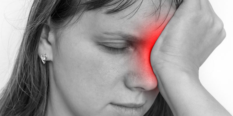 A black and white image of a person with their hand on their eye. The eye area has been coloured in red to signify pain.