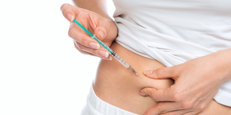 Photograph showing someone pinching their stomach area with one hand and the other holding an injection ready to self administer their injection.