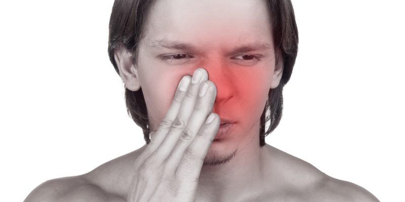 Image of a person with their hand against their nose with a painful expression on their face.