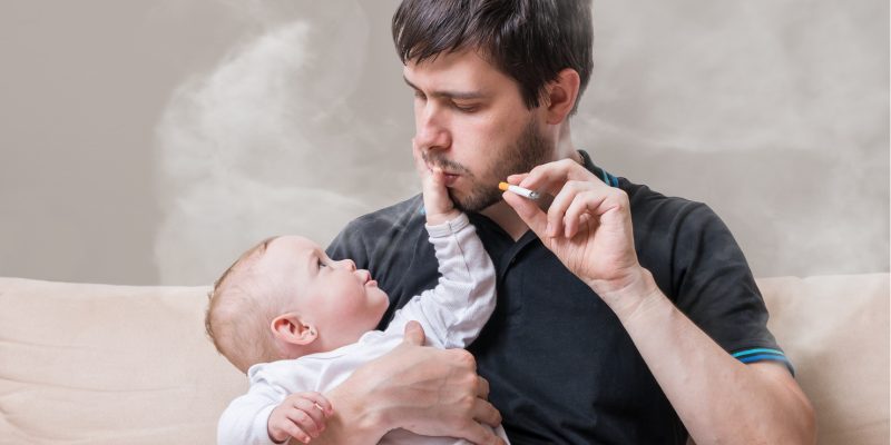 Image showing a person smoking whilst holding a baby. Smoke is in the air for the baby to breath in.