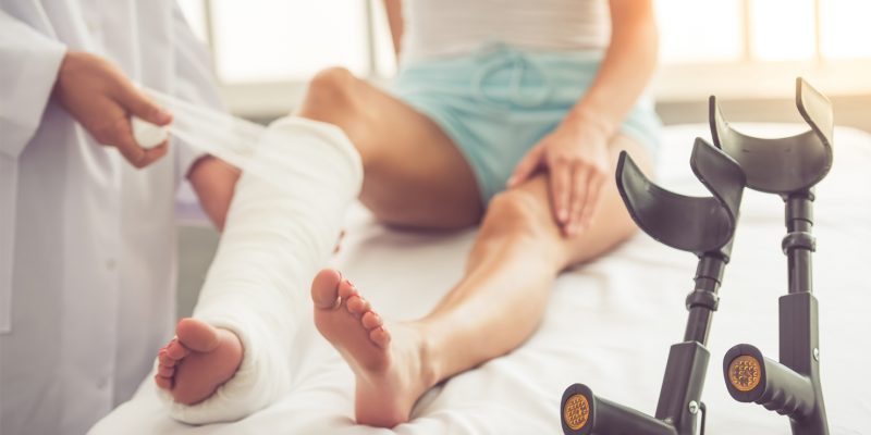 Photograph of a doctor putting a plaster cast on a patients right leg.