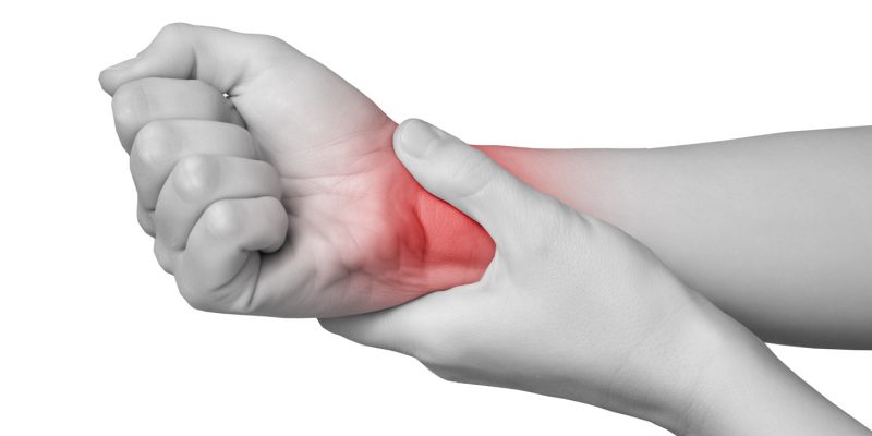 Black and white image showing someone holding their hand and wrist. The base of the hand and wrist area is coloured red to signify pain