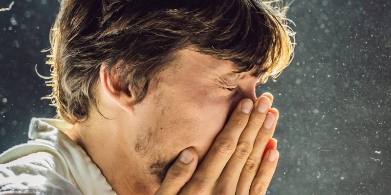 A person sneezing, in the background there are lots of dust particles in the air.