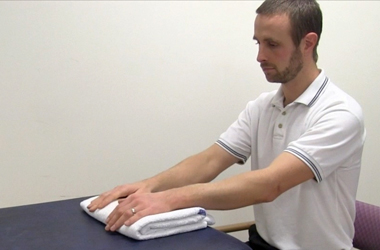 Sat at a table, both hands are placed on a folded towel on the table top