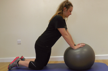 Side view - Kneeling on the floor with both hands placed on the top of the ball, elbows out straight