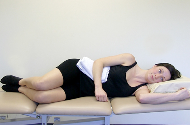 Lying in a side position with a towel placed between the waist and elbow - the arm is resting on the towel