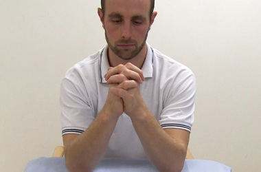 Elbows are placed on the table with palms touching and fingers interlocked