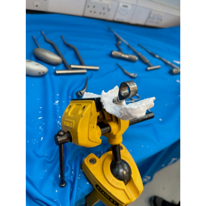 A yellow vise holding a 3D modelled joint with a metal pin sticking out of it.