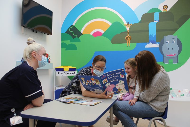 Young girl reading a book with staff on the children's pre-assessment unit