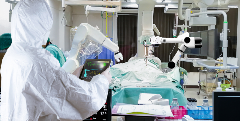 A surgeon using a robotic arm to operate on a patient while research nurses stand in the background.