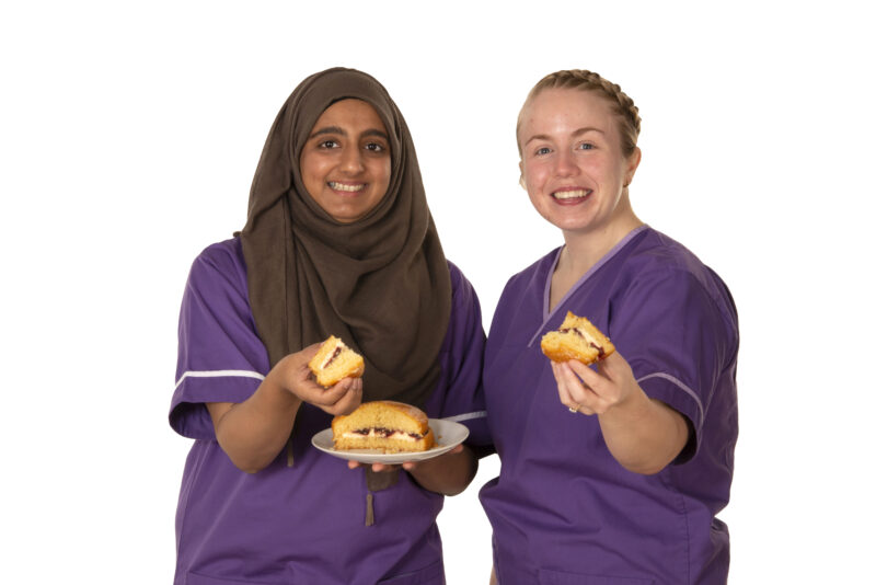 Two dietitians holding a plate of cake, with a slice of cake each in their other hands. 