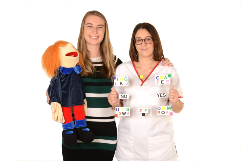 Two speech and language therapists,  holding a puppet and letter cards. 