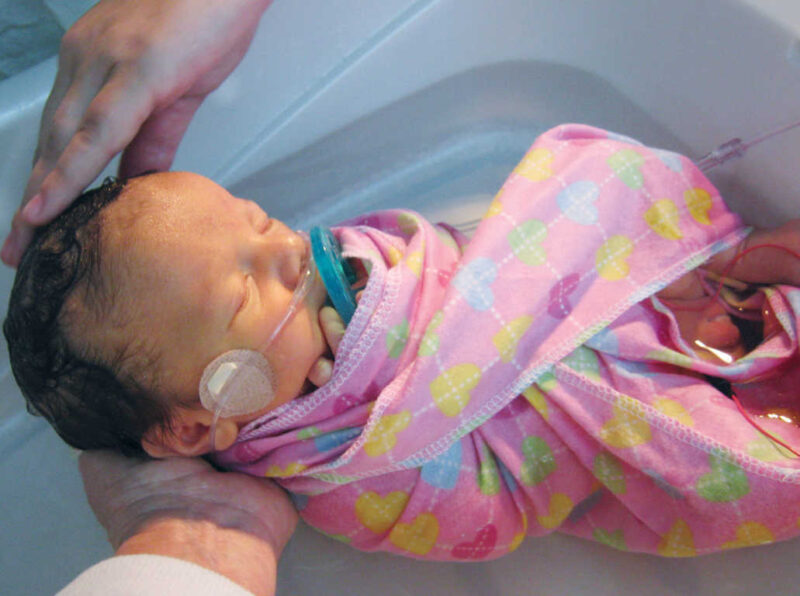 Baby on oxygen with dummy in mouth, wrapped in a muslin cloth whilst being bathed