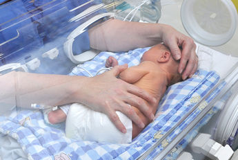 Baby laid on side with person laying hand on head and hand on body 