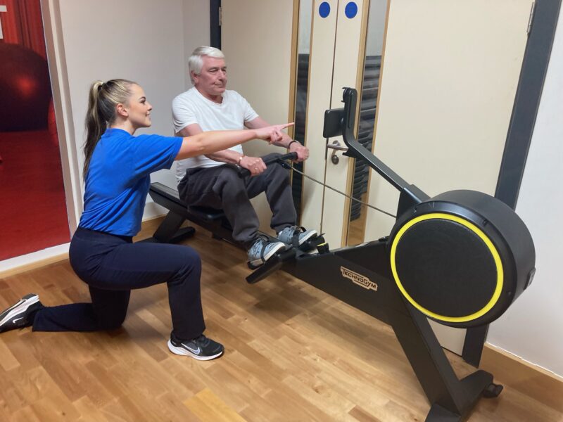 An instructor working with a patient doing exercise on a rowing machine.
