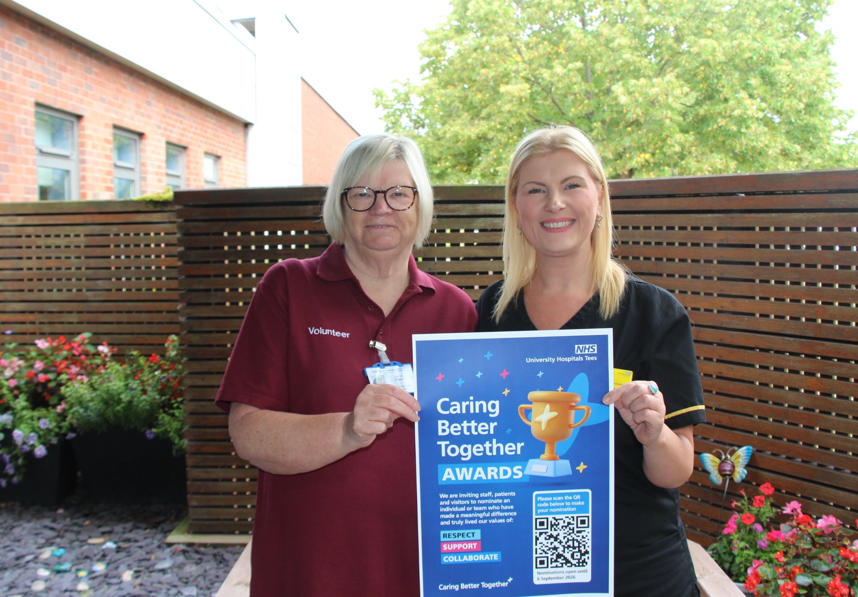 Two University Hospitals Tees volunteers holding a Caring Better Together awards poster