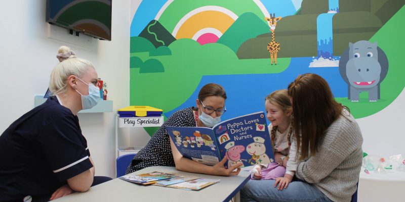 Young patient reading a book with staff at James Cook's pre assessment unit